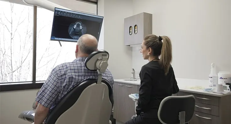 A patient in the dental chair reviewing a scan on the screen with a team member